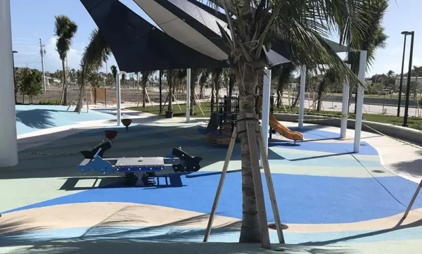 Commercial playground with pebble flex rubber safety flooring, shade structure, and colorful non-slip surface in a public park.