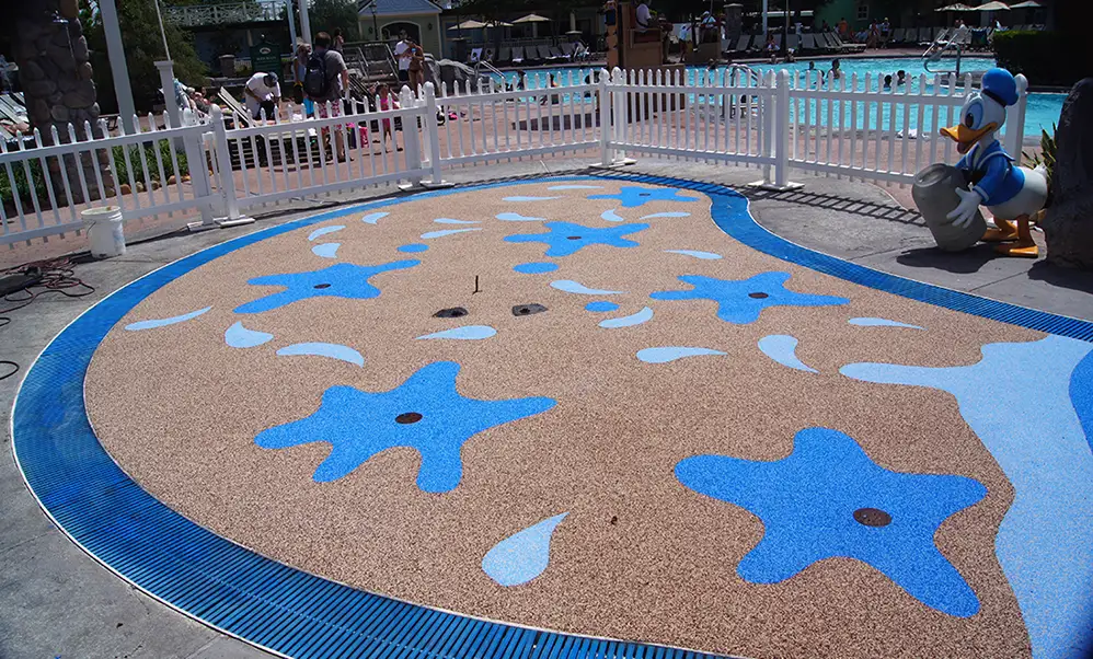Commercial splash pad surface with blue water splash design and non-slip rubber flooring at a resort pool area.
